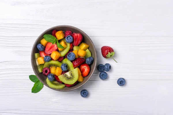 健康的でダイエット生活のための天然有機食品 キウイ イチゴ ブルーベリー ラズベリー ミントの白木の背景で新鮮なフルーツサラダのトップビュー — ストック写真