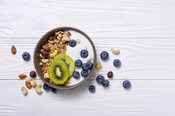 健康と食事の朝食のための有機食品 グラノーラとボウルのトップビュー ヨーグルト 新鮮なキウイ 白木の背景にブルーベリーとナッツ — ストック写真