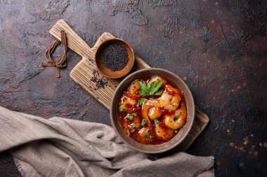 Acı biber soslu baharatlı karides ve koyu beton arkaplanda siyah susam tohumları.