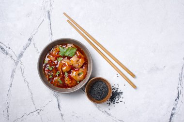 Baharatlı karides ve acı biber soslu siyah susam tohumları ve beyaz mermer arka planda yemek çubukları.