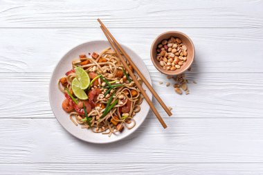 Asya usulü erişte, baharatlı karides, kızarmış tofu peyniri, fıstık, limon ve yeşil soğanlı beyaz ahşap zemin.