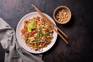 Asya usulü erişte, baharatlı karides, kızarmış tofu peyniri, yer fıstığı, limon ve yeşil soğanlı koyu beton arkaplan.