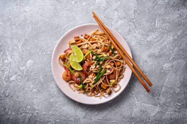 Asyalı udon eriştesi, baharatlı karides, kızarmış tofu peyniri, fıstık, limon ve yeşil soğanlı gri beton arka plan.