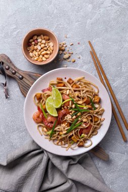 Asyalı udon eriştesi, baharatlı karides, kızarmış tofu peyniri, fıstık, limon ve yeşil soğanlı gri beton arka plan.