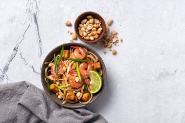 Asya usulü erişte, baharatlı karides, kızarmış tofu peyniri, fıstık, limon ve yeşil soğanlı beyaz mermer zemin.