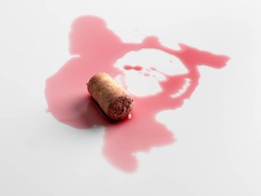 Kırmızı şarap mantarı ve dökülen sıvı ışık arka planında soyut bir leke oluşturuyor. Minimalist kompozisyonda kaza, kusur ve sembolik zarafet kavramı.