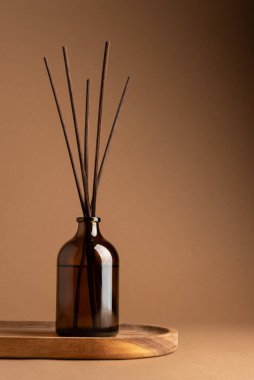 Tahta tepside kahverengi kamışlı Amber cam aroma yayıcı, nötr arkaplanda minimalist ürün sergisi. Rahatlama, denge ve doğal ev kokusu kavramı.