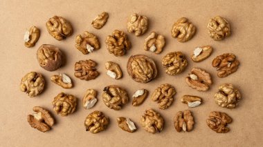 Kahverengi arka plana saçılmış çiğ ceviz çekirdeklerinin üst görüntüsü. Doğal sağlıklı atıştırmalık konsepti organik gıda, sadelik ve kırsal dokuyu sembolize eder..