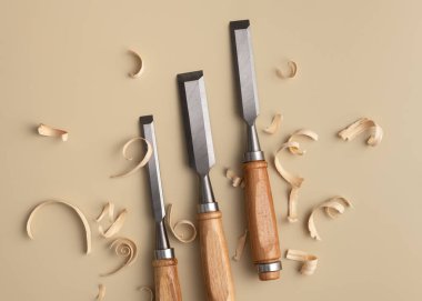 Bej arka planda ahşap talaşı olan üç ahşap keski seti. Minimalist zanaatkar sahnesi beceri, hassasiyet ve el yapımı ahşap estetiği vurguluyor.