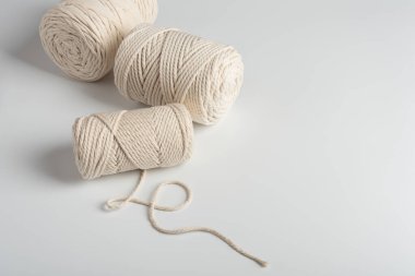 Temiz beyaz arka planda doğal pamuk tokaları olan el yapımı makrome ip. DIY projeleri, dokuma, boho dekoru ve tekstil yaratıcılığı için Rustik araç gereçleri.