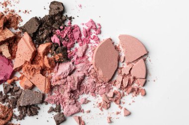 Ezilmiş çok renkli göz farı tozu beyaz bir yüzeye saçılmış. Pembe, şeftali rengi ve parlak desenli kahverengi kozmetik palet. Marka ve reklamlar için güzellik makyaj arka planı.