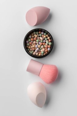 Pastel makyaj süngerleri ve temiz bir arka planda fırçası olan renkli toz incileri. Kozmetik, cilt bakımı, kadınlık, yumuşak makyaj ve kişisel bakım temaları için minimum güzellik düzlüğü.