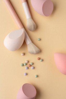 Pastel makyaj süngerleri, fırçalar ve sıcak bir zemine yerleştirilmiş toz incileri. Kozmetik, cilt bakımı, kadınlık, spa ve yumuşak makyaj rutin temaları için minimum güzellik kompozisyonu.