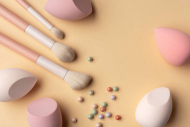 Pastel makyaj süngerleri, fırçalar ve sıcak bir zemine yerleştirilmiş toz incileri. Kozmetik, cilt bakımı, kadınlık, spa ve yumuşak makyaj rutin temaları için minimum güzellik kompozisyonu.