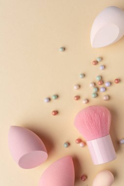 Sıcak pastel arka planda yumuşak makyaj süngerleri, fırça ve toz incileri. Sakin tonlarda temiz güzellik kavramı, yumuşak dokular, minimal kompozisyon, ve cilt rutini ve modern estetiğe odaklan..