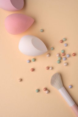 Pastel makyaj süngerleri, fırçalar ve sıcak bir zemine yerleştirilmiş toz incileri. Kozmetik, cilt bakımı, kadınlık, spa ve yumuşak makyaj rutin temaları için minimum güzellik kompozisyonu.