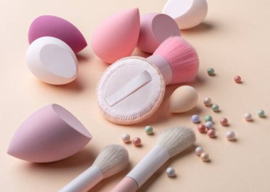 Makyaj aletleri ve kozmetik tozu incileri yumuşak pastel arka planda sıralanmış. Doğal ışıltı, kadınlık, cilt bakımı ve günlük makyaja odaklı yumuşak güzellik konsepti.