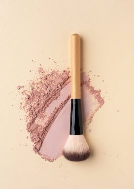 Makyaj fırçası ve pastel arka planda yumuşak toz lekesi. Kozmetik uygulamayı, dokuyu ve zarafeti gösteren temiz asgari güzellik kavramı, cilt bakımı, markalaşma, editoryal veya reklam kullanımı için mükemmel.