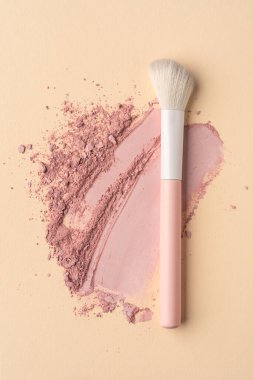 Makyaj fırçası ve pastel arka planda yumuşak toz lekesi. Kozmetik uygulamayı, dokuyu ve zarafeti gösteren temiz asgari güzellik kavramı, cilt bakımı, markalaşma, editoryal veya reklam kullanımı için mükemmel.