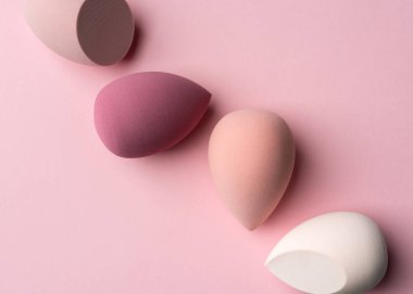 Makyaj süngerlerinin yumuşak pembe tonlarda olduğu asgari soyut güzellik arka planı. Güzellik ve tasarım kavramları için sakin, yumuşak, kadınsı ve modern estetik idealleri ifade eden temiz kozmetik kompozisyonu.