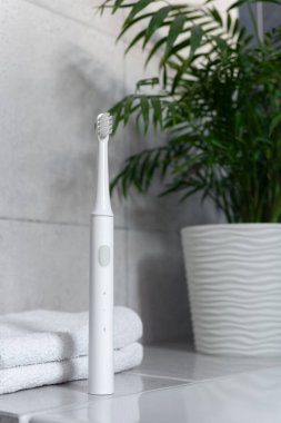 Minimalist banyo içinde havlu ve bitkilerle birlikte modern ultrasonik diş fırçası. Günlük kişisel bakım, sağlık rutini, hijyen, temiz yaşam tarzı ve sakin sabah ya da akşam ritüeli kavramı.