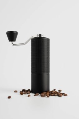 Açık arkaplanda kahve çekirdekleri olan siyah bir el değirmeni. Kahve ayinini, sakin işçiliği, hassasiyeti ve modern günlük basitliği vurgulayan temiz, sade bir hayat..
