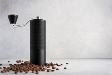 Açık arkaplanda kahve çekirdekleri olan siyah bir el değirmeni. Kahve ayinini, sakin işçiliği, hassasiyeti ve modern günlük basitliği vurgulayan temiz, sade bir hayat..