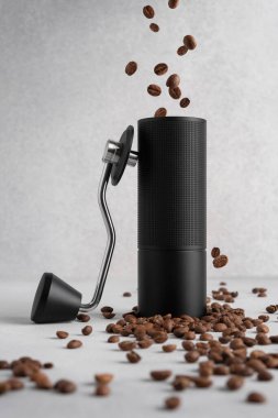 Hafif arka planda dağınık kahve çekirdekleri olan siyah bir el değirmeni. Temiz modern hayat tazeliği, hareketi, kahve ritüelini ve ustalığı ön plana çıkarıyor..