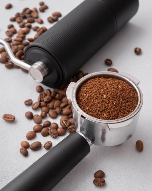 Elle kahve öğütücü, kavrulmuş fasulye ve hafif arka planda öğütülmüş kahve ile doldurulmuş portafilter. Özel kahve, ustalık, hassasiyet ve dikkatli demleme ritüeli kavramı..