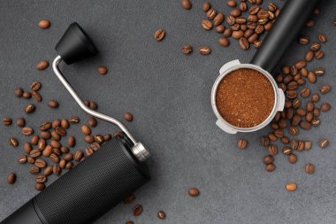 Manüel kahve öğütücüsünün üst görüntüsü, öğütülmüş kahve ile dolu portafilter, ve koyu dokulu arkaplanda kavrulmuş fasulye. Profesyonel kahve akışı, hassasiyet, denge ve hazırlık kavramı.