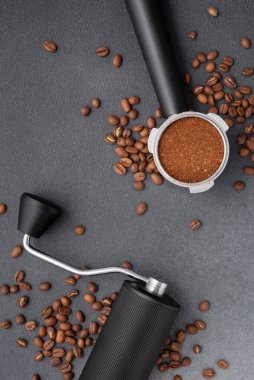 Manüel kahve öğütücüsünün üst görüntüsü, öğütülmüş kahve ile dolu portafilter, ve koyu dokulu arkaplanda kavrulmuş fasulye. Profesyonel kahve akışı, hassasiyet, denge ve hazırlık kavramı.