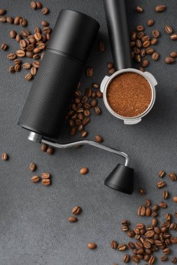 Manüel kahve öğütücüsünün üst görüntüsü, öğütülmüş kahve ile dolu portafilter, ve koyu dokulu arkaplanda kavrulmuş fasulye. Profesyonel kahve akışı, hassasiyet, denge ve hazırlık kavramı.