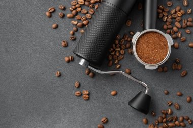 Manüel kahve öğütücüsünün üst görüntüsü, öğütülmüş kahve ile dolu portafilter, ve koyu dokulu arkaplanda kavrulmuş fasulye. Profesyonel kahve akışı, hassasiyet, denge ve hazırlık kavramı.