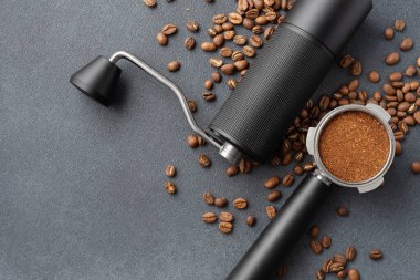 Manüel kahve öğütücüsünün üst görüntüsü, öğütülmüş kahve ile dolu portafilter, ve koyu dokulu arkaplanda kavrulmuş fasulye. Profesyonel kahve akışı, hassasiyet, denge ve hazırlık kavramı.