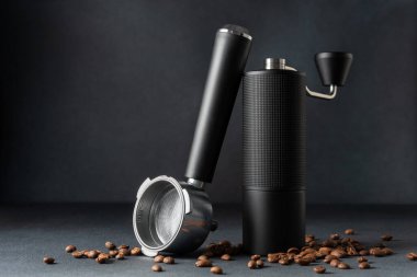 El yapımı kahve öğütücü ve koyu arkaplanda kavrulmuş fasulyeli espresso filtresi. Minimum lüks hala kahve ritüeli, işçilik, hassasiyet ve odaklanmış analog yaşam tarzı vurguluyor..