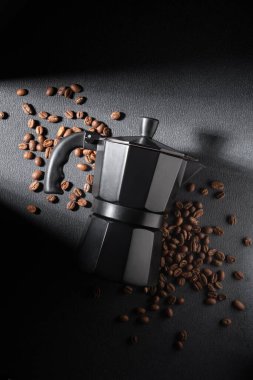 Koyu bir zemin üzerinde koyu kahve çekirdekleri olan siyah moka demliği dramatik bir şekilde sert ışıkta. Huysuz hayat, kahve ayinini, yoğunluğu, işçiliği ve kaliteli estetiği ön plana çıkarıyor..