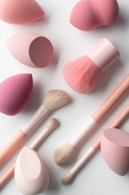 Makyaj fırçaları ve açık arkaplanda yumuşak pembe tonlarda kozmetik süngerler. Profesyonel araçları, kişisel bakım rutinini, kadınlığı ve modern asgari estetiği vurgulayan temiz güzellik kavramı.