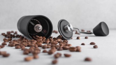 Hafif arkaplana saçılmış kavrulmuş kahve çekirdekli siyah manuel kahve öğütücüsü. Özel kahveyi, ustalığı, hassasiyeti, yavaş ritüeli ve özgün ev yapımı deneyimini simgeleyen minimum natürmort yaşam.