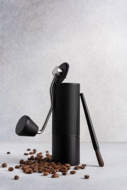 Hafif arkaplana saçılmış kavrulmuş kahve çekirdekli siyah manuel kahve öğütücüsü. Özel kahveyi, ustalığı, hassasiyeti, yavaş ritüeli ve özgün ev yapımı deneyimini simgeleyen minimum natürmort yaşam.