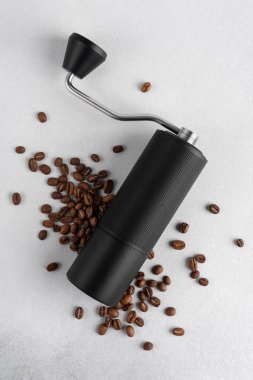 Hafif arkaplana saçılmış kavrulmuş kahve çekirdekli siyah manuel kahve öğütücüsü. Özel kahveyi, ustalığı, hassasiyeti, yavaş ritüeli ve özgün ev yapımı deneyimini simgeleyen minimum natürmort yaşam.