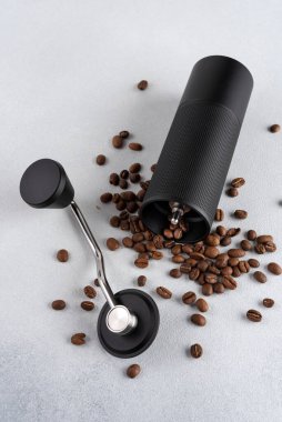 Hafif arkaplana saçılmış kavrulmuş kahve çekirdekli siyah manuel kahve öğütücüsü. Özel kahveyi, ustalığı, hassasiyeti, yavaş ritüeli ve özgün ev yapımı deneyimini simgeleyen minimum natürmort yaşam.