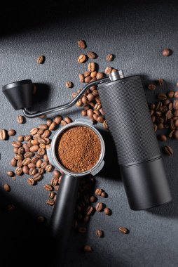 Koyu dokulu arka planda öğütülmüş kahve ile doldurulmuş el yapımı kahve öğütücü ve iskele filtresi. Moody ışıklandırması espresso hazırlığını, kahve ustalığını ve özel kahve ritüelini ön plana çıkarıyor..