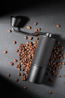 Koyu dokulu arkaplanda kavrulmuş fasulye ile elle kahve öğütücü. Huysuz dramatik ışıklandırma, kahve hazırlamada işçilik, ritüel ve kontrolün altını çizer. Özel kahve ve yaşam tarzı kavramları için ideal..