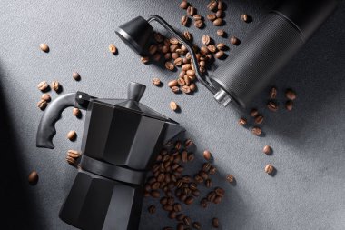 El yapımı kahve öğütücüsü ve koyu dokulu kavrulmuş fasulyeli siyah moka demliği. Karamsar ışıklandırma geleneksel espresso ritüelini, zanaatkarlığı ve kaliteli ev yapımı atmosferi vurguluyor.