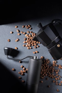 El yapımı kahve öğütücüsü ve koyu dokulu kavrulmuş fasulyeli siyah moka demliği. Karamsar ışıklandırma geleneksel espresso ritüelini, zanaatkarlığı ve kaliteli ev yapımı atmosferi vurguluyor.