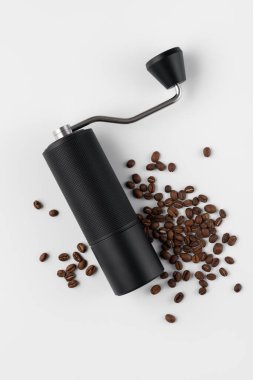 Hafif arkaplana saçılmış kavrulmuş kahve çekirdekli siyah manuel kahve öğütücüsü. Özel kahveyi, ustalığı, hassasiyeti, yavaş ritüeli ve özgün ev yapımı deneyimini simgeleyen minimum natürmort yaşam.