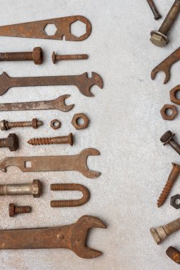 Gri desenli arka planda eski paslı anahtarlar, cıvatalar ve fındıklar var. Antika metal aletler, atölye atmosferi ve kopyalama alanı ile endüstriyel onarım ve bakım kavramı.