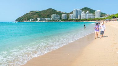 Sanya Çin, 25 Mart 2021: Çinli turistler Sanya Hainan adasında güneşli bir günde Dadonghai beyaz kumsalında çıplak ayakla yürüyorlar.