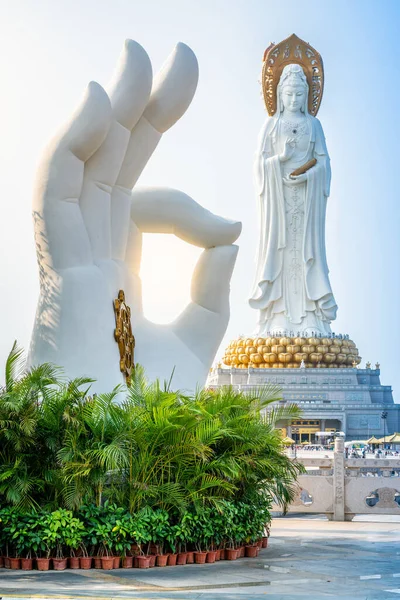 Vertical view of white hand statue with Dharma wheel and Guanyin of the South Sea statue in the background at Nanshan Buddhism cultural park temple in Sanya in Hainan island China