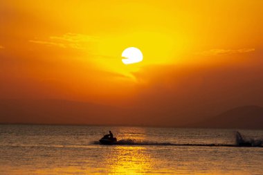 Jet ski ve denizin üzerinde altın güneş. Denizin üzerinde muhteşem bir gün batımı. Altın bir günbatımının arka planında jet ski süren bir turist. Güzel manzara, jet ski 'de bir adam, deniz ve gün batımı.